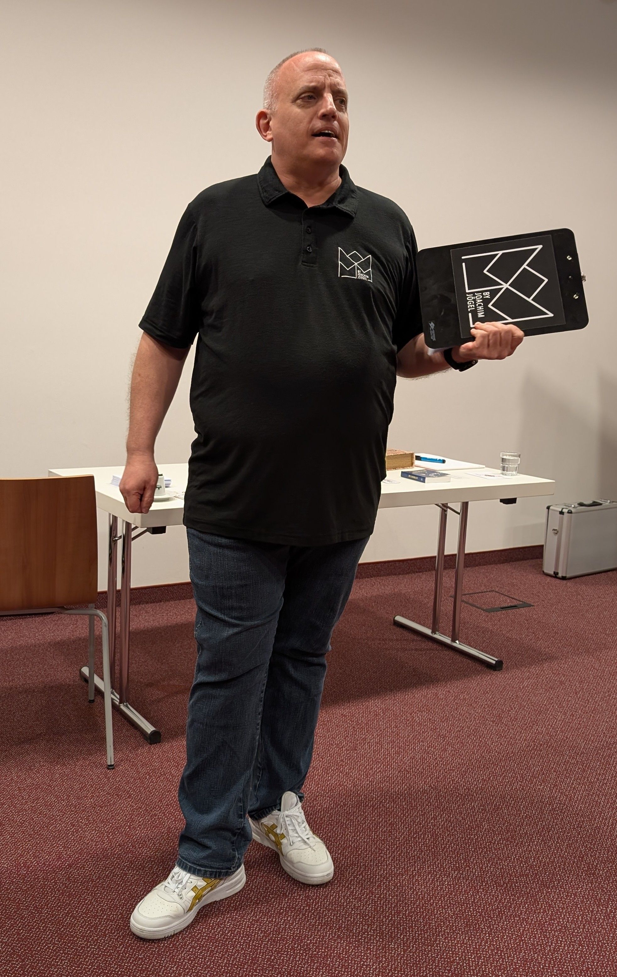 Joachim Jögel bei einem Vortrag vor Firmenpublikum, mit einer Klemmbrett-Requisite in der Hand